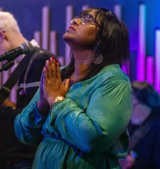 A woman worshipping with her hands together during a Sunday service