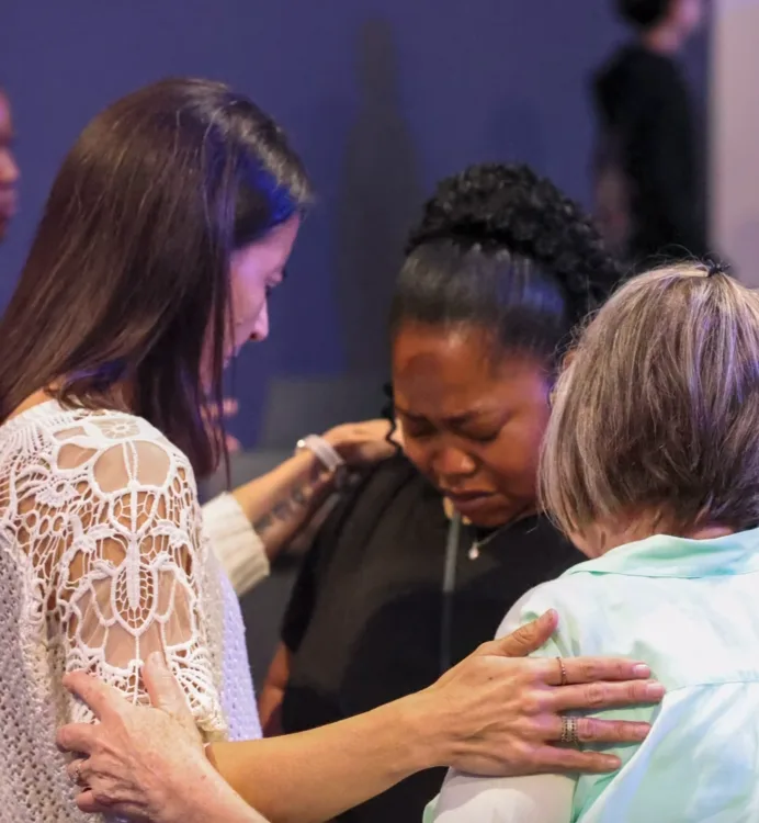Three women praying together, hands on each other’s shoulders