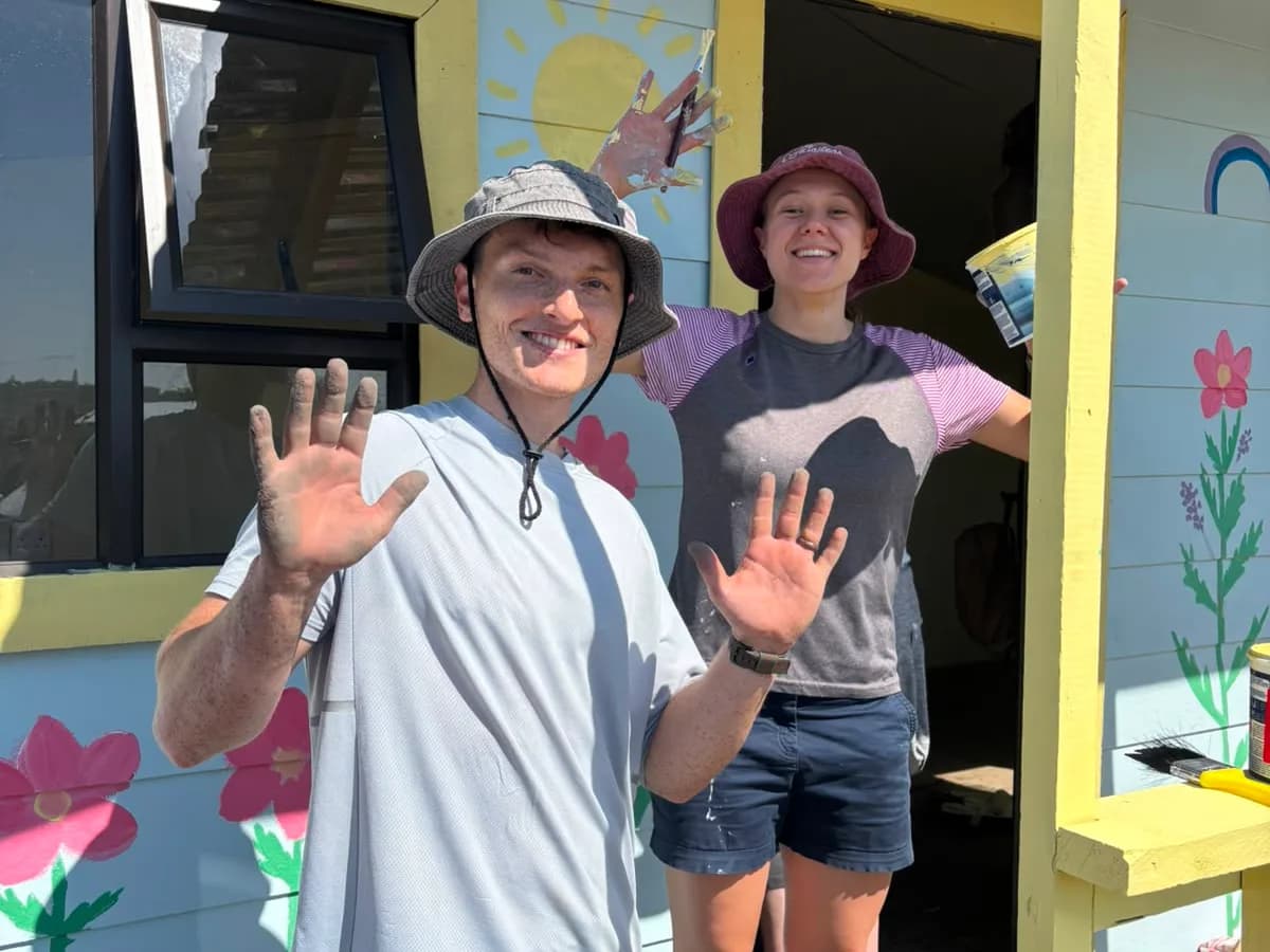 Two volunteers with paint on their hands outside a house they have just painted